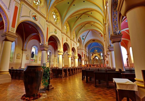 Interior of a colorful church featuring arched ceilings, wooden pews, and decorative murals.