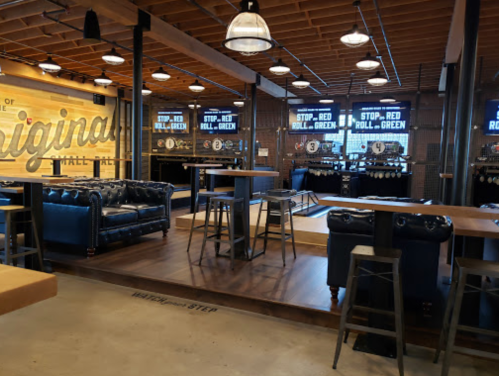 Interior of a modern bar with leather seating, wooden tables, and large screens displaying messages.