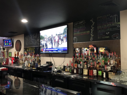 A bar with a variety of liquor bottles on the counter and a TV displaying news in the background.