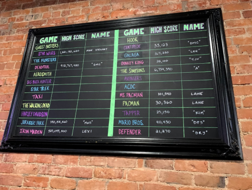 A chalkboard displaying high scores for various arcade games, including titles like Star Wars, Pacman, and Iron Maiden.