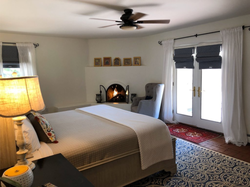 Cozy bedroom with a bed, lamp, armchair, and fireplace, featuring light curtains and a patterned rug.