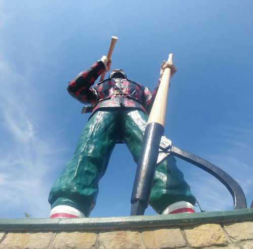 A towering statue of a lumberjack holding two large logs against a clear blue sky.