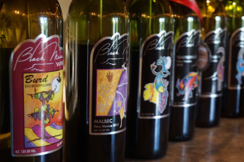A row of wine bottles with colorful labels, showcasing various types like Malbec and Burd from Black Mesa Winery.