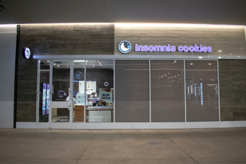 Exterior of an Insomnia Cookies store with a "Now Open" sign, featuring large glass windows and a modern design.