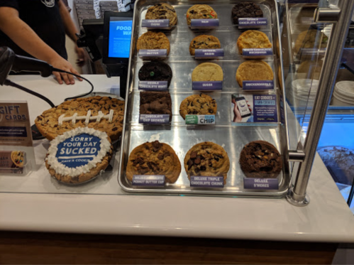 A display case filled with various cookies, including chocolate chip, peanut butter, and s'mores, next to a cookie pie.