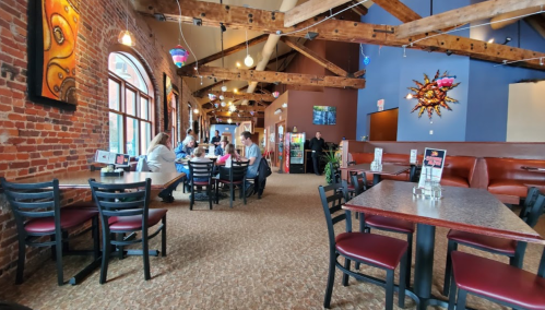 Interior of a restaurant with exposed brick walls, wooden beams, and patrons dining at tables. Brightly lit and inviting atmosphere.