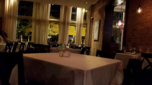 A dimly lit restaurant interior with a table set for dining, featuring large windows and brick walls.