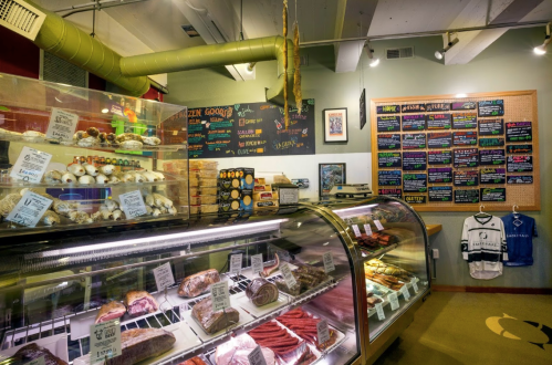 A colorful deli display with various meats and pastries, featuring a chalkboard menu and vibrant decor.