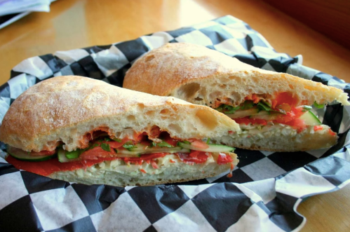 A freshly cut sandwich with layers of vegetables, served on a black and white checkered paper.