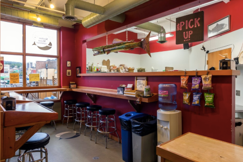 A cozy eatery with red walls, bar seating, a fish decoration, and a water cooler near a trash can.