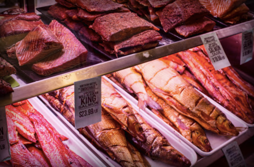 Display of various smoked fish, including salmon and other seafood, with price tags visible.