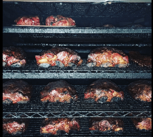 Smoked meats on multiple racks in a smoker, showcasing a variety of dark, caramelized textures.