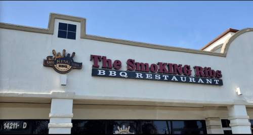 Sign for "The SmoKING Ribs BBQ Restaurant" with a crown logo, located on a light-colored building.