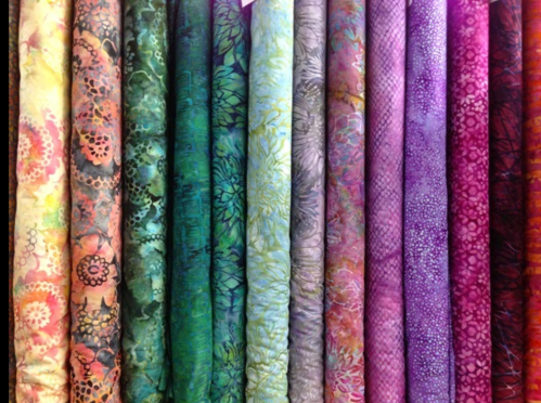 A colorful display of rolled fabrics in various patterns and textures, featuring vibrant hues of blue, pink, and green.