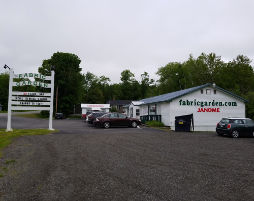 Sign for Fabric Garden with a building and parking area, featuring Janome branding and a website address.