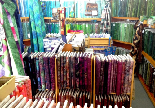 A vibrant fabric store filled with colorful rolls of patterned fabric arranged on shelves and tables.