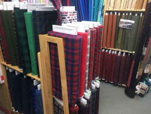 A display of colorful fabric rolls in various patterns, including plaid, arranged on shelves in a craft store.