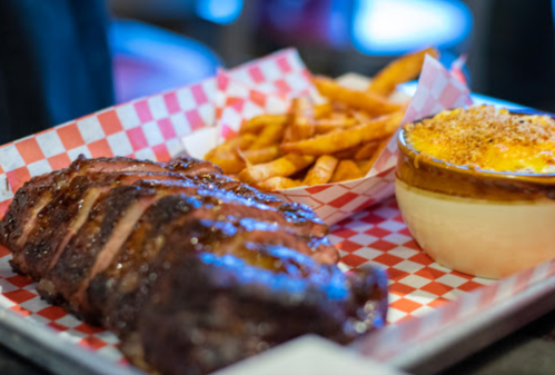 A platter featuring sliced barbecue ribs, seasoned fries, and a bowl of creamy macaroni and cheese.