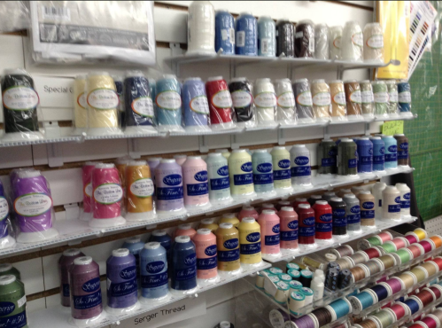 A display of colorful spools of thread arranged neatly on shelves in a craft store.
