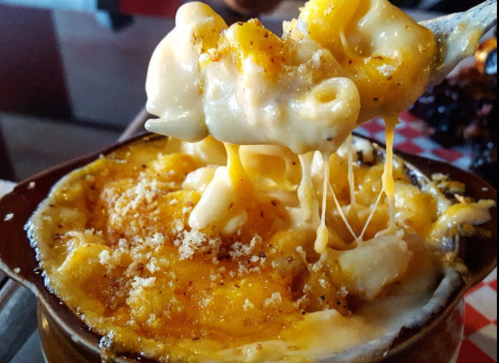 A creamy, cheesy macaroni and cheese dish with a golden, crispy topping, served in a bowl with a fork lifting a portion.