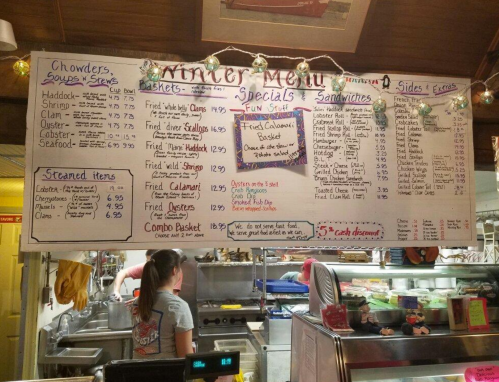 A winter menu featuring chowders, seafood, sandwiches, and specials, displayed on a large board in a restaurant.