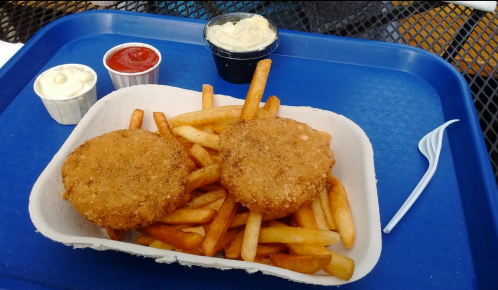 Two golden-brown chicken patties on a bed of fries, accompanied by three dipping sauces in small cups.