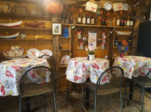 Cozy restaurant interior with lobster-themed tablecloths, wooden decor, and shelves of wine and nautical items.