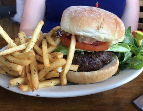 A juicy hamburger with lettuce, tomato, and onion, served with a side of crispy French fries and a small salad.