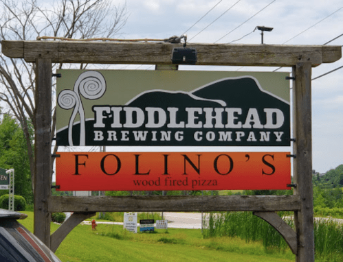 Sign for Fiddlehead Brewing Company and Folino's Wood Fired Pizza, featuring mountains and a colorful gradient background.
