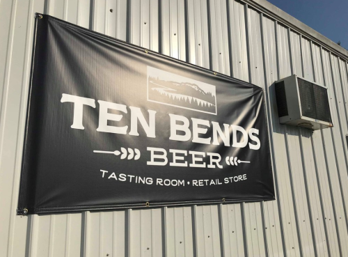 Sign for "Ten Bends Beer" featuring a tasting room and retail store, displayed on a metal building.