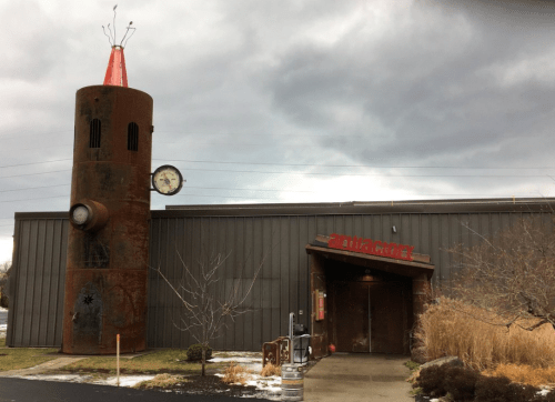 A rustic building with a tall, rusty tower and a red cone on top, featuring a large clock and the word "attraction."