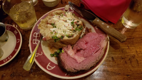 A plate with a baked potato topped with sour cream and green onions, alongside a slice of roast beef.