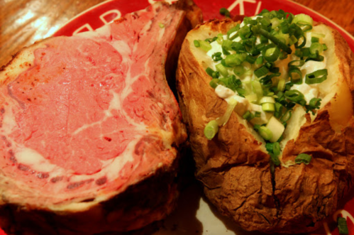 A plate featuring a juicy prime rib and a baked potato topped with sour cream and chopped green onions.
