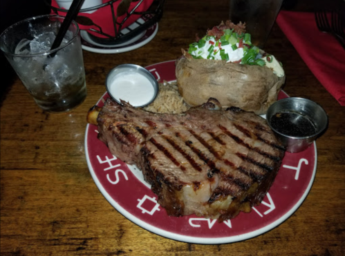 A grilled pork chop on a plate with a baked potato topped with sour cream and chives, and a side of rice.