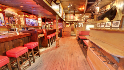 A rustic bar interior with wooden decor, red stools, and a moose head mounted on the wall. Warm, inviting atmosphere.