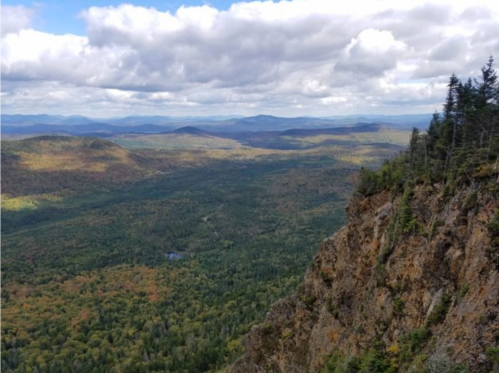 A panoramic view of a lush green valley surrounded by mountains under a partly cloudy sky.