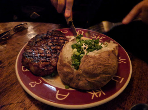 A grilled steak and a baked potato topped with green onions on a decorative plate.