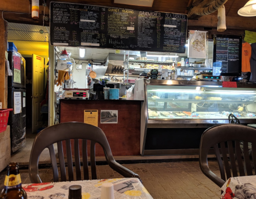 A cozy restaurant interior featuring a menu board, display case with food, and tables with chairs.
