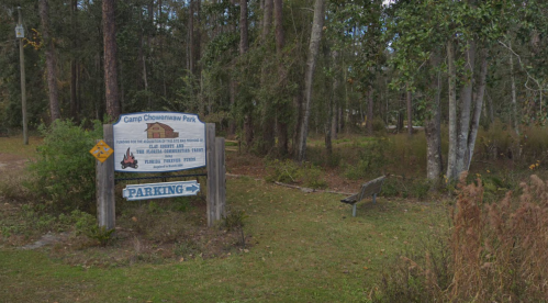 Sign for Camp Chocowinity Park, surrounded by trees, with a parking area visible nearby.