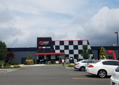 A modern building with a checkered pattern, featuring a sign for an indoor racing facility, surrounded by parked cars.