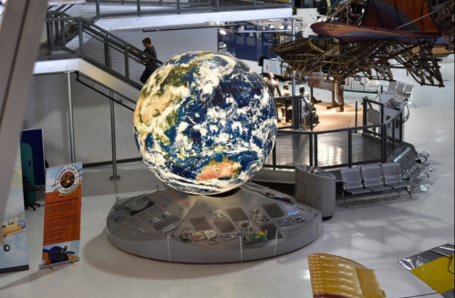 A large globe of Earth displayed in a museum, surrounded by exhibits and seating areas.