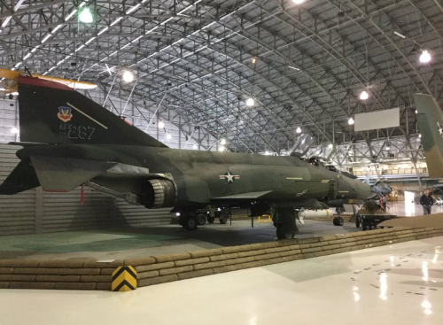 A military aircraft displayed inside a large hangar with a high ceiling and various equipment in the background.