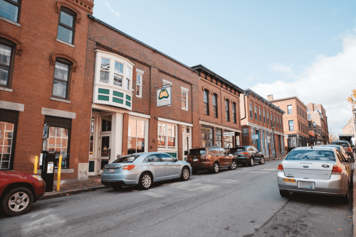 A charming street lined with brick buildings and parked cars under a clear blue sky.