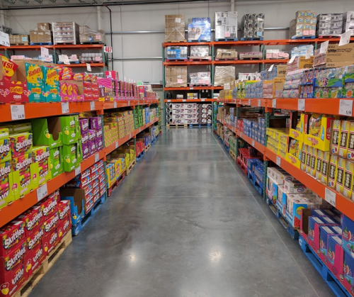 A wide aisle in a warehouse store lined with colorful boxes of snacks and candy on shelves.