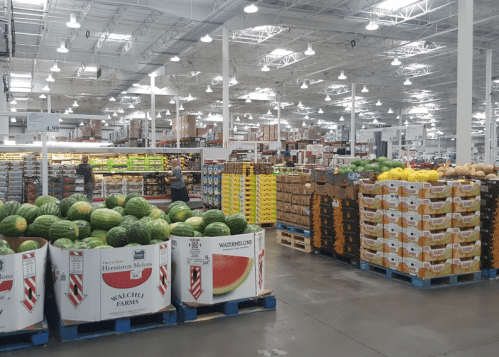 A spacious warehouse store with displays of watermelons and various fruits in organized stacks. Brightly lit interior.