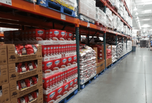 A warehouse aisle filled with stacked boxes of rice and other bulk food items on pallets.