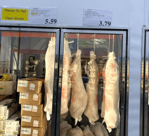 Two hanging meat cuts in a display case with price tags: $5.59 and $3.79. Boxes are stacked below.