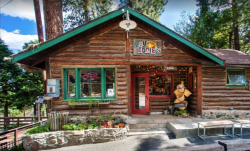 A rustic log cabin restaurant with an "Open" sign, surrounded by trees and decorated with lights.