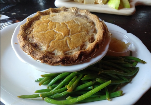 A savory pie in a white dish, served with green beans and a small cup of applesauce on the side.