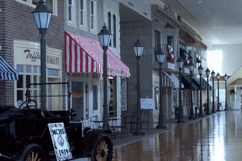 A vintage street scene with shops, striped awnings, and a classic car in a well-lit indoor setting.